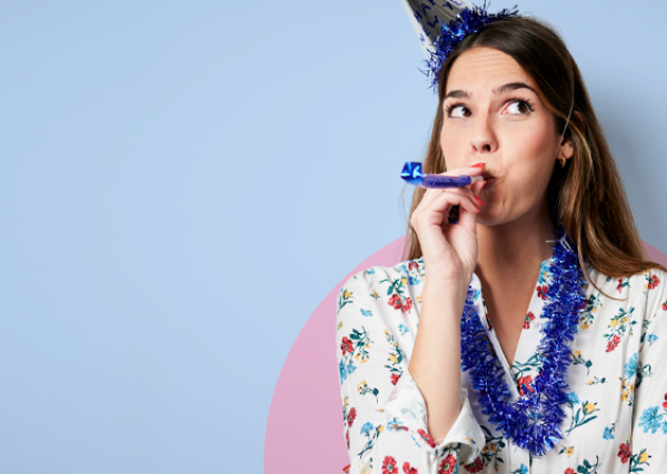 A woman wears a party hat and blows on a noise maker to celebrate